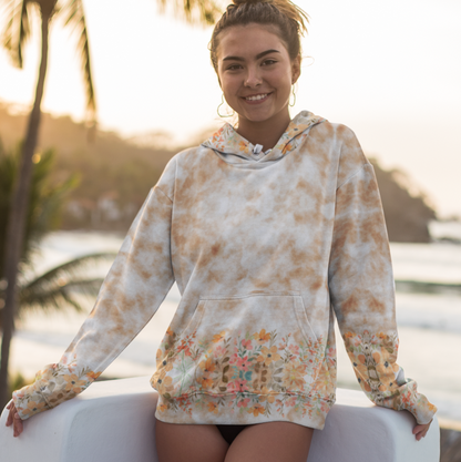 A woman wearing the Fall Flowers in Brown Tie Dye Beach Hoodie Cozy Sweatshirt by Chameleon Surf, standing on a sandy beach with the ocean in the background. The unisex hoodie features a vibrant brown tie-dye print with autumn flower patterns, soft fabric, and a relaxed fit, perfect for chilly beach evenings.